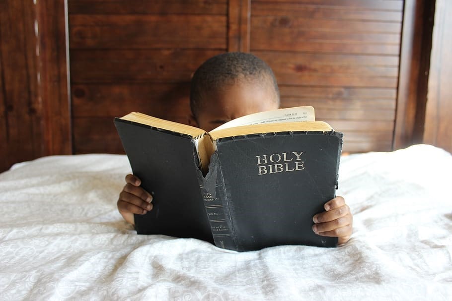 Child reading bible in bed