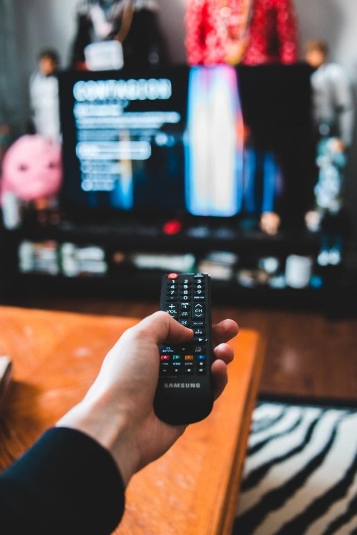 person pressing remote control button to watch movie